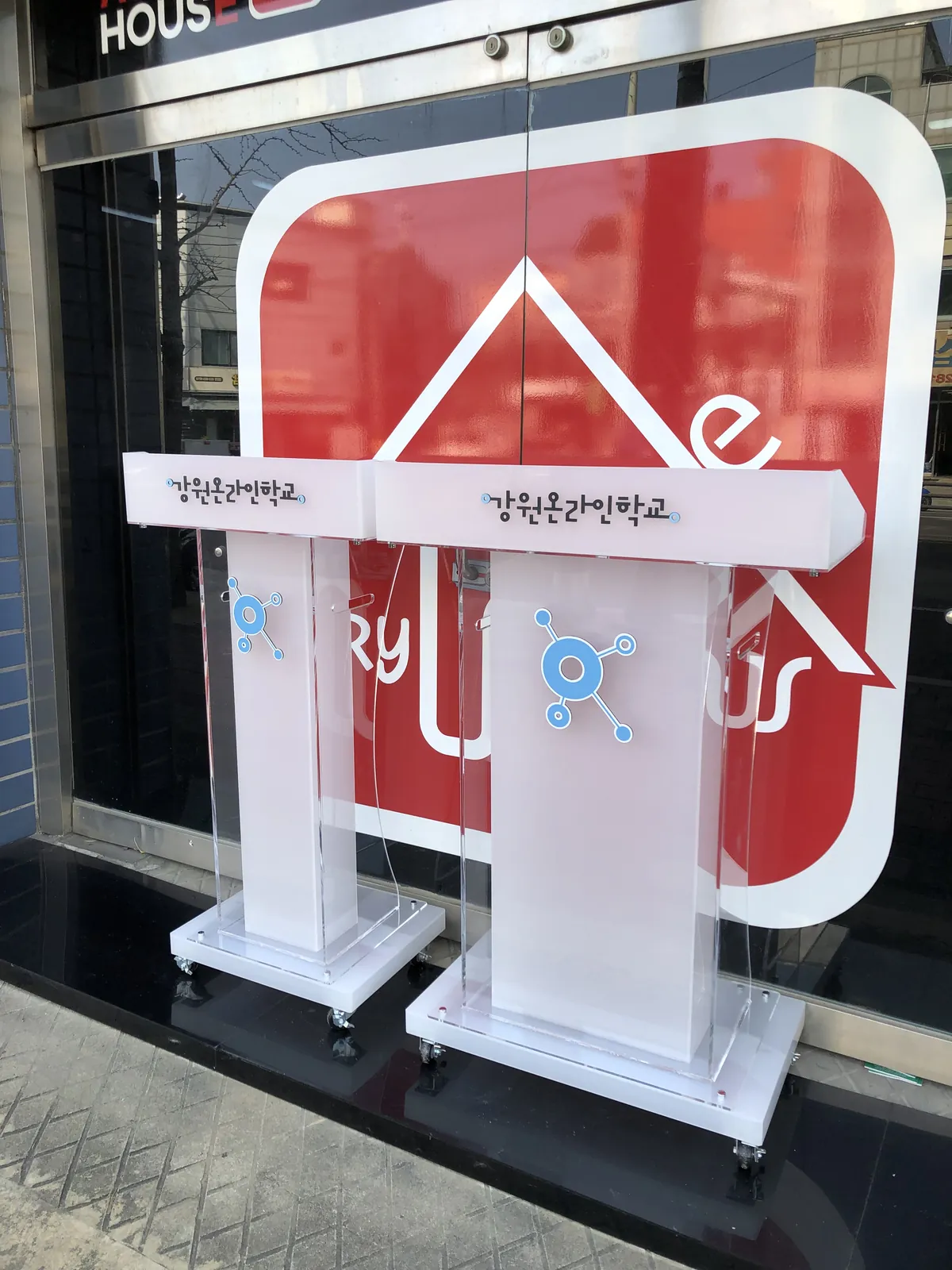 서리 아크릴로 통일하고 파란 로고와 학교 이름을 넣은 강원온라인학교 아크릴 강연대와 사회대, 하단에 바퀴가 달려 있습니다